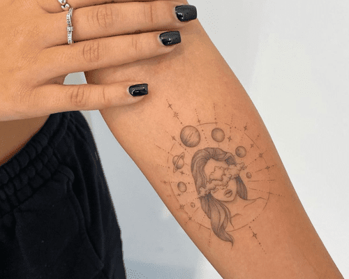 A forearm with a compass tattoo design featuring the planets and a woman's face with clouds over her eyes