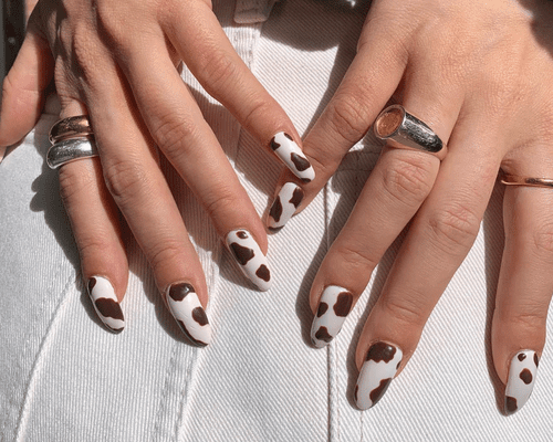 A close up of white nails with brown cow print art.