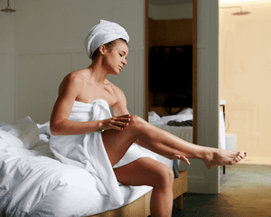 Woman in a towel applying lotion to her legs