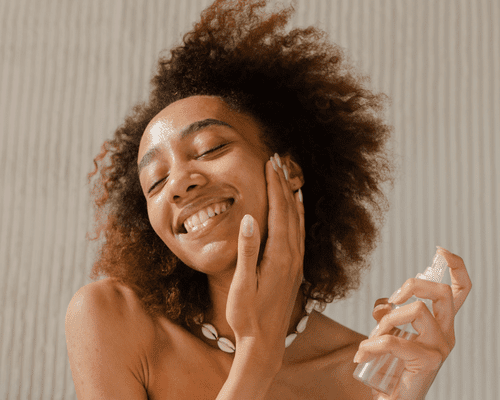 A woman smiling as she sprays her face with a facial mist