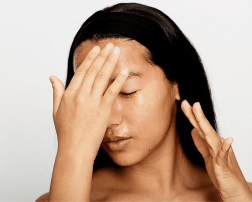 Close up of a model rubbing her face with both hands.