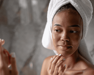 Woman in a towel examining her skin in the mirror with her hand on her chin