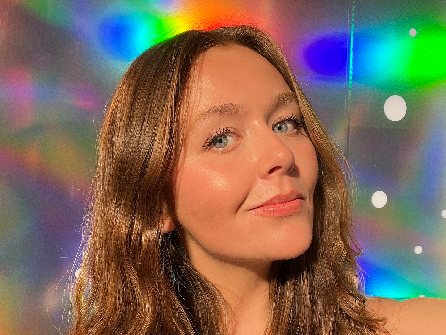 close up of woman with glowy makeup on rainbow background