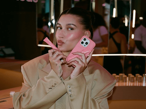 Hailey holding a lip gloss and phone. 