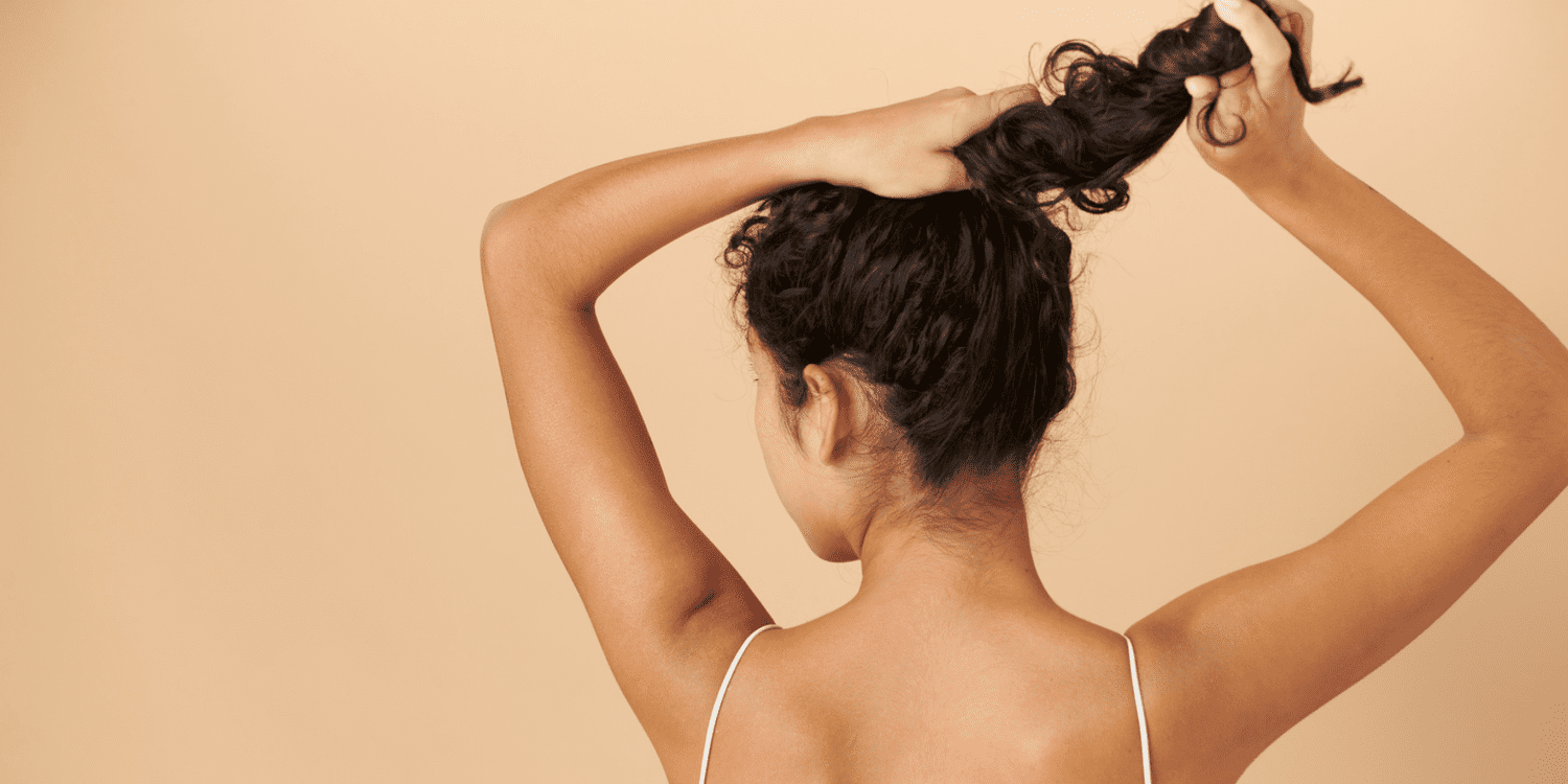 The back of a woman's head as she holds the base and lengths of her ponytail