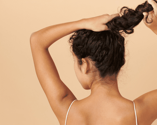 The back of a woman's head as she holds the base and lengths of her ponytail