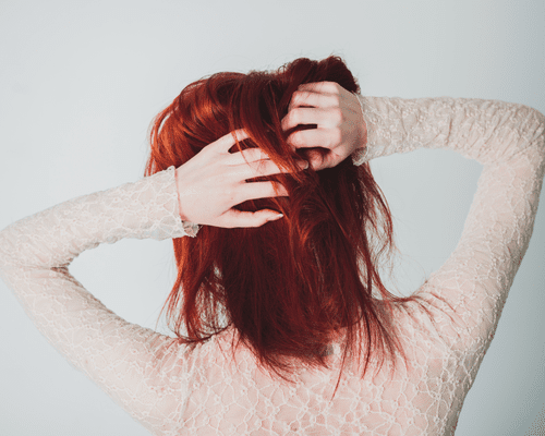 The back of a woman's head and her touching her red hair with her hands