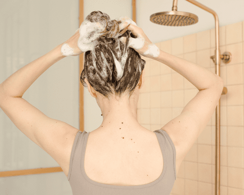 A woman in the shower with suds in her hair as she washes it