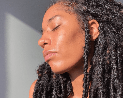 A woman with the sun hitting her face and locs in her hair