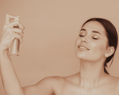 A woman with her eyes closed misting a makeup setting spray onto her face