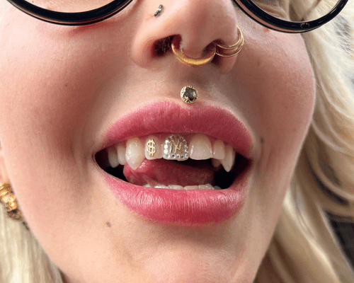 Half of a woman's face with multiple nose piercings, tooth gems, and a medusa piercing