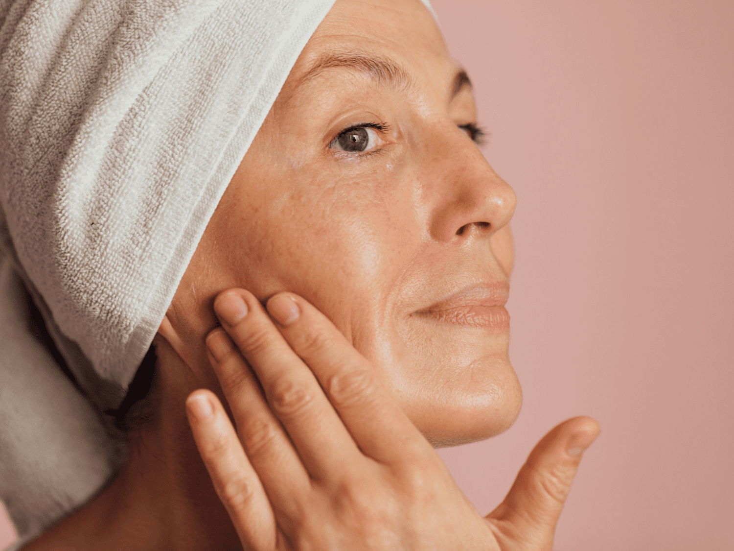 A woman with clean skin and her hair in a towel touching her face