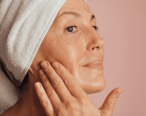 A woman with clean skin and her hair in a towel touching her face