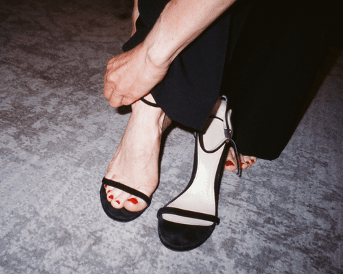 A woman's feet with red painted toenails as she puts her foot in sandal heels