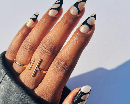 A hand with painted nails that have a black and sparkly white design