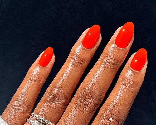 close up of bright red gel manicure on dark background