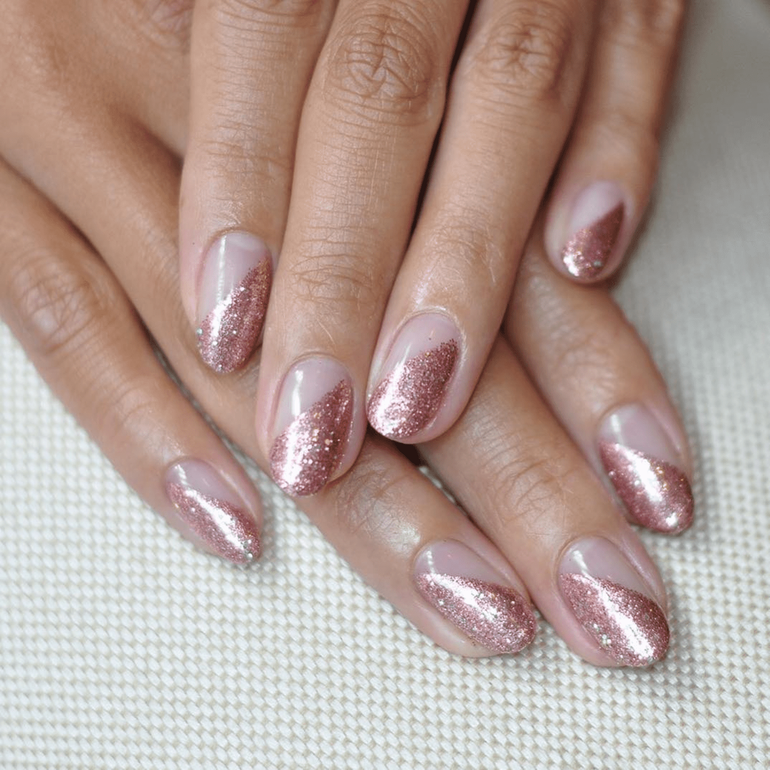 Nude nails with diagonal stripes of rose gold glitter nail polish.