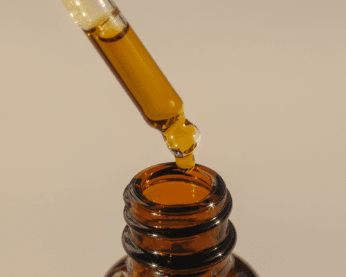 close up of golden oil dropper on tan background