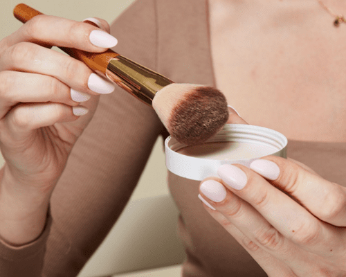 woman tapping makeup brush on powder lid