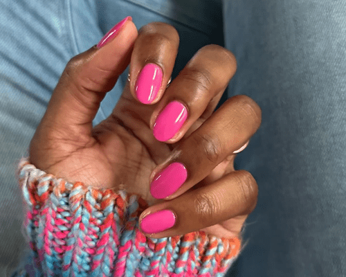 A hand with hot pink short nails and the sleeve of a rainbow sweater