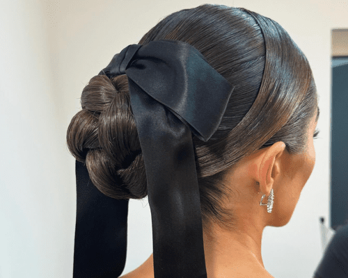 The side profile of Olivia Culpo with a slick back braided bun and big black bow