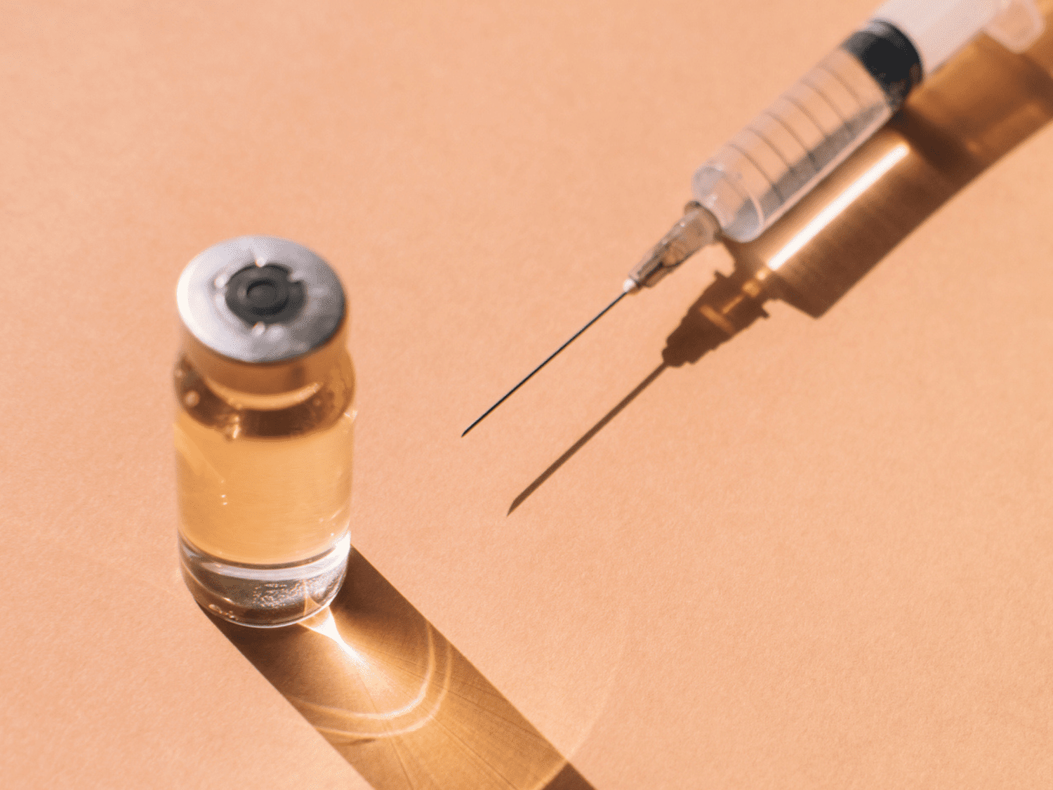 Close up of a syringe and clear vial on an orange background.