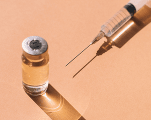 Close up of a syringe and clear vial on an orange background.