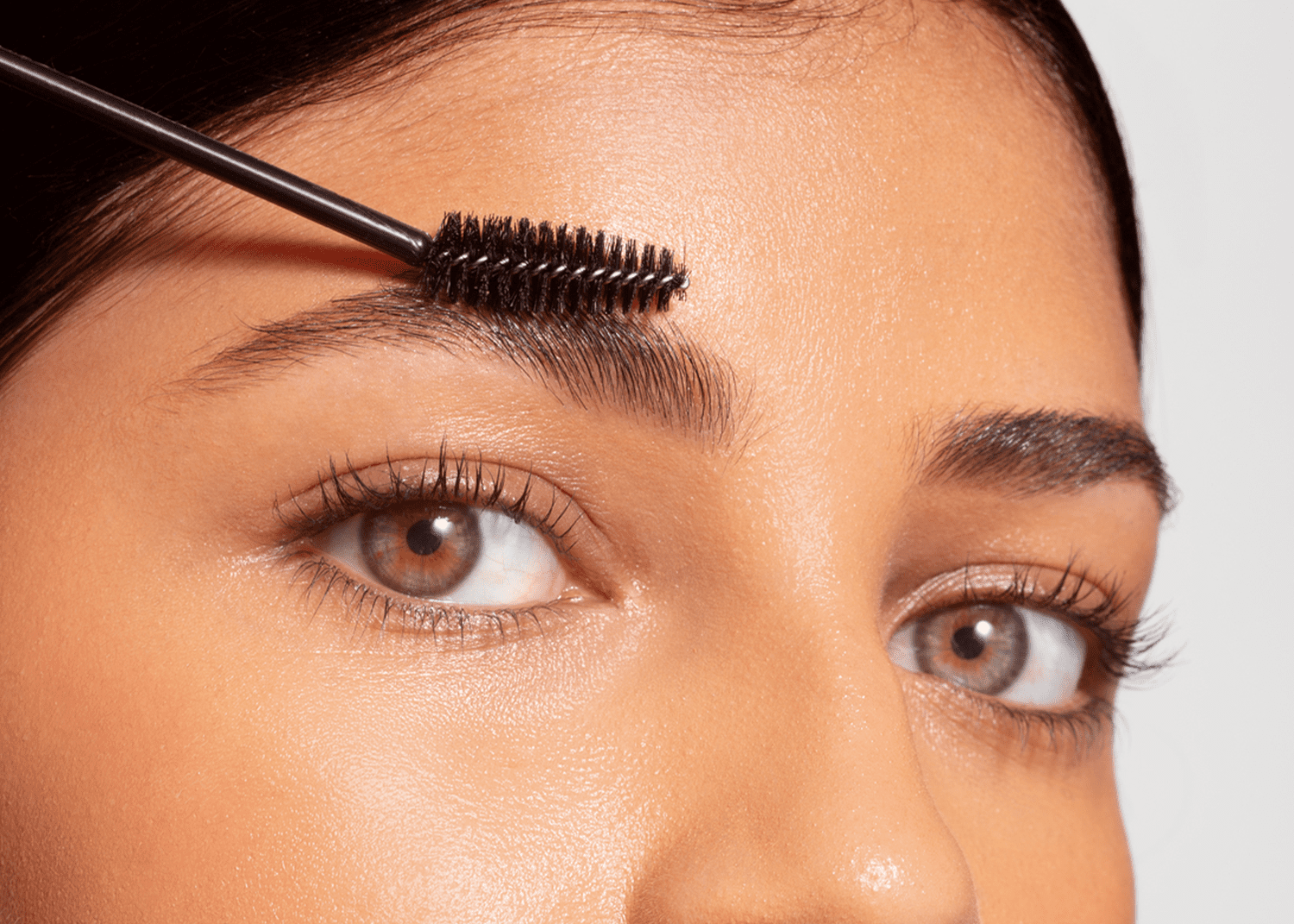 close up of woman combing spoolie brush through eyebrows