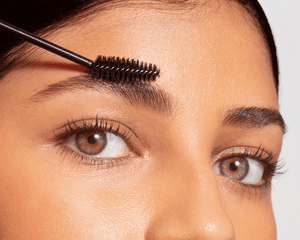 close up of woman combing spoolie brush through eyebrows